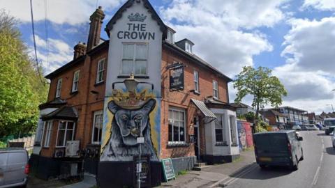 External shot of The Crown in Billericay. A mural of an animal wearing a crown is painted on one wall of the building, which sits on the corner of a road 