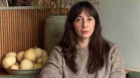 A woman with long dark brown hair looks sadly at the camera