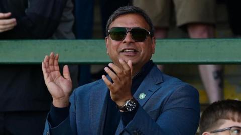 Prabhu Srinivasan standing in the stand at Huish Park clapping his hands