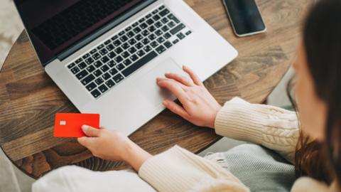A person holding a credit card on a laptop.