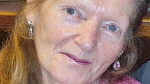 Rose Johnston, who has blue eyes, long wavy red hair, is wearing pink ear-rings, smiles at the camera