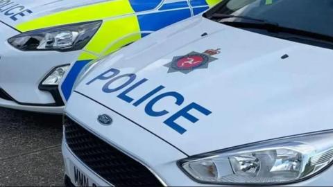 The bonnet of a Manx police car reading POLICE in capital letters. It is parked next to another.