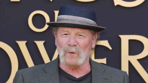 Peter Mullan, an actor on the red carpet at an award event. He has a white beard and thinning hair.