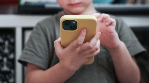 Close up of  a child holding yellow smartphone, he is wearing a grey t-shirt.