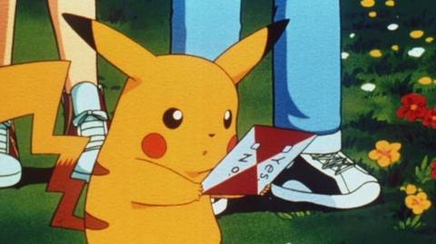An image of a yellow Pokémon character with long pointed ears and red cheeks. it is holding a piece of paper.