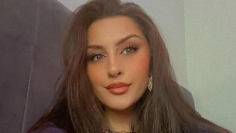 Madia Kauser with long brown hair, hazel eyes, wearing gold earrings and toffee coloured lipstick.