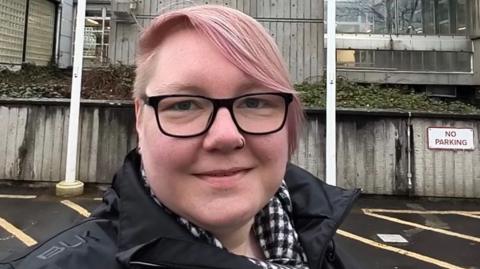 A woman with pink dyed hair standing in front of a council office