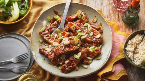 A bowl of slow cooker pork belly, topped with spring onions and toasted sesame seeds.