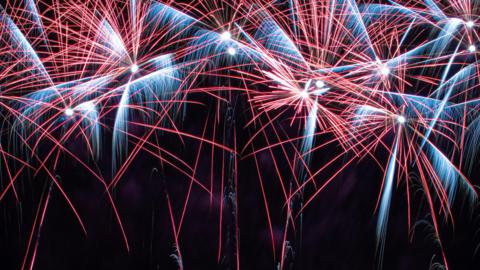 Red, orange and blue fireworks explode against the black night sky