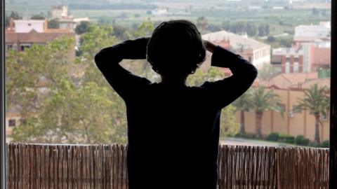 A little boy looks out of a window at his home in Godella, Valencia, Spain