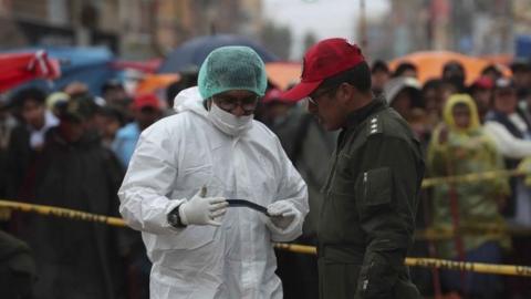 Bolivian police and a member (L) of the Scientific Technical Research Institute of the Police University (IITCUP) inspect the scene an explosion a day before, that caused six dead and 28 injured in a street market that remains cordoned off while the investigation continues in the city of Oruro, Bolivia, 11 February 2018.