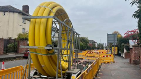 A large coil of yellow plastic piping for gas works on Heavitree Road in Exeter with yellow plastic barriers placed around it.