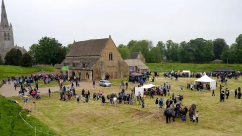 Oakham Castle surrounded by visitors and stalls. A man on horseback can be seen inside a large pen.