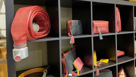 A shelf with a hose, handbags and purses sitting alongside