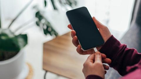 A person holding a black mobile phone in their hand while inserting a white charger.