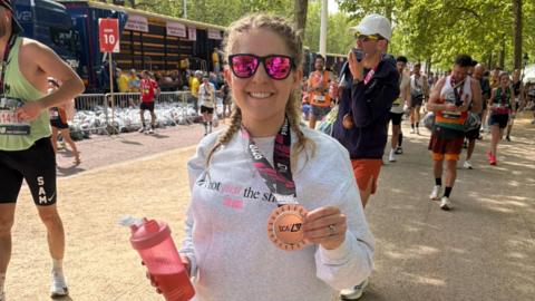 Gabriella smiling and holding up her finisher's medal.