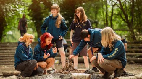 A group of Explorer scouts making a camp fire in a wooded clearning