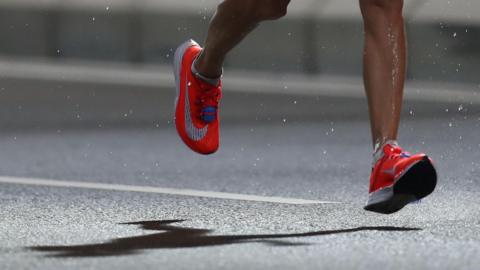A man in a pair of bright red Nike trainers runs on tarmac on a rainy day.