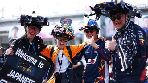 Fans wear hats designed like cars and give a thumbs up in the fanzone at Suzuka 