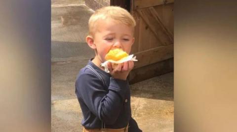 A small blond-haired boy eating a piece of cake.