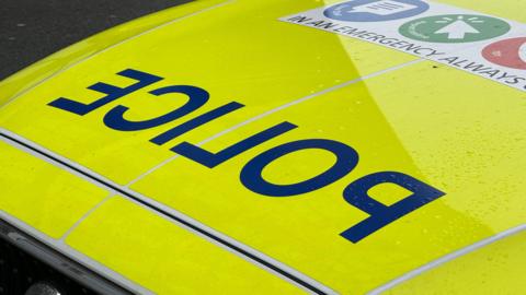 The bonnet of a police car, with the word POLICE in reverse lettering in navy blue on a yellow high visibility background.
