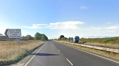 The A15 dual carriageway with a sign pointing to the Elsham Wolds Industrial Estate. The sky is blue with some clouds.