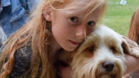 A picture of Ruth Szymankiewicz, who has long ginger hair, cuddling a terrier dog.