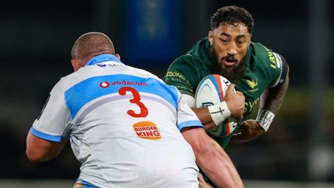 A rugby player runs with the ball in his hand and prepares for contact with a tackling defender