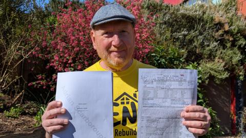 A man wearing a yellow t-shirt and a cap. He is standing outside and holding call sheet for the show's final ever scene. 