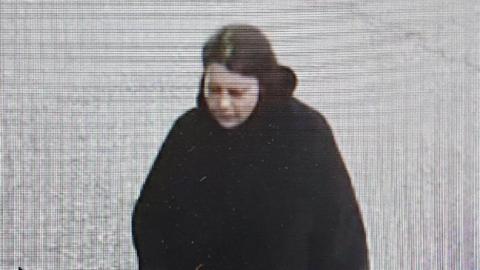 A grainy CCTV image of a woman with dark hair in a dark coat