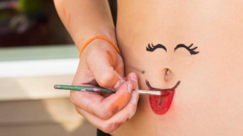 Photograph of a smiley face being drawn around a belly button