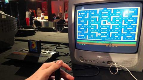 Image shows hand at the controls of an Atari game console playing Pac-Man on a Panasonic television