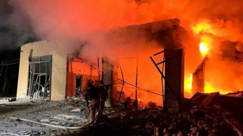 Fire in a building that has been burnt down as firefighter holds hose in the foreground.