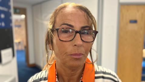 Dawn Style, a woman wearing glasses and a shirt with an orange collar, is stood in a corridor.