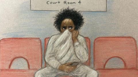 A court sketch of a young man with curly dark hair holding his jumper up over his mouth and nose. 