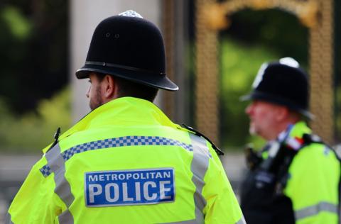 Two male police officers wearing high viz yellow jackets and helmets. One is pictured back view, the other side view.