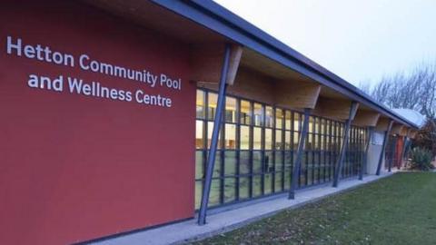 A picture of the front of Hetton Community Pool, it is a long one story building with lots of glass panels through which you can just see the pool 