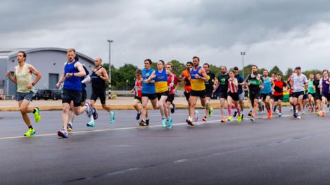 A group of runners running on a airfield runway