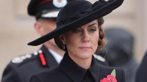 Princess of Wales, wearing a black coat and hat with service personnel behind her