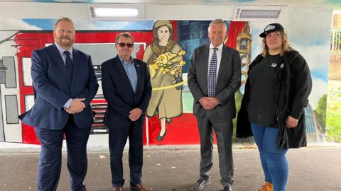 A picture of Adrian Hawkins, Cllr Richard Henry, Cllr Phil Bibby and street artist Szylk Wane in front of a part of the mural depicting the Queen's visit to Stevenage in 1959.