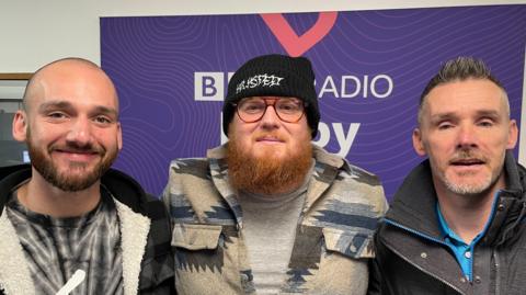 Three men with beards, one wearing a hat and glasses