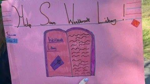 A banner made by a child with an image of a book and the words help save Westbrook Library.
