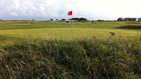Golf course with red flag standing in hole and long grass bordering the fairway.