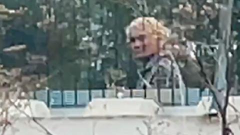 A zoomed in image taken from our undercover filming of a Vietnamese people smuggler, hair dyed blonde, walking behind a fence