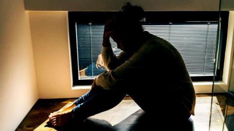 A stressed person sitting on the floor holding their forehead in their palm