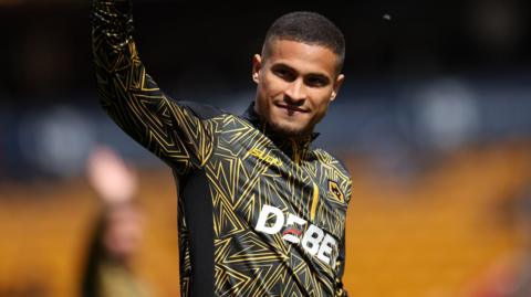 A photo of Joao Gomes waving at the crowd at the Molineux wearing his black and gold Wolves warm-up top in May