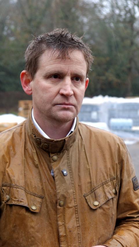 A man in a brown coat. There are crates of bottled water behind him.