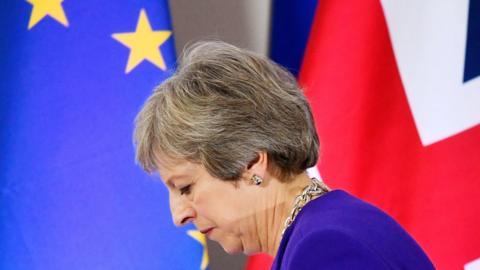 The British and EU flags behind Theresa May, who is looking down