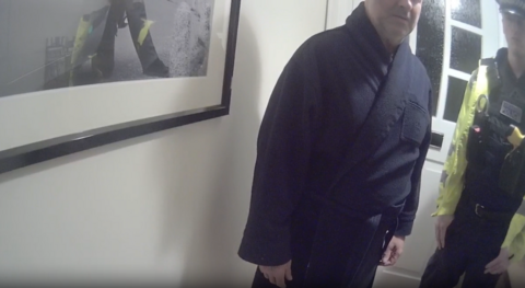 A man in a dressing gown stood in a hall way next to a police officer.