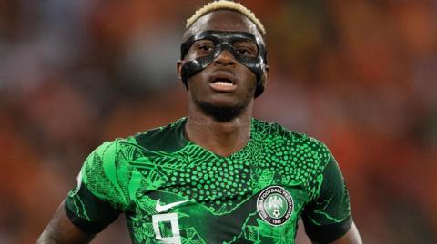 Victor Osimhen wears a protective black eye mask and a green Nigeria shirt during a football match.